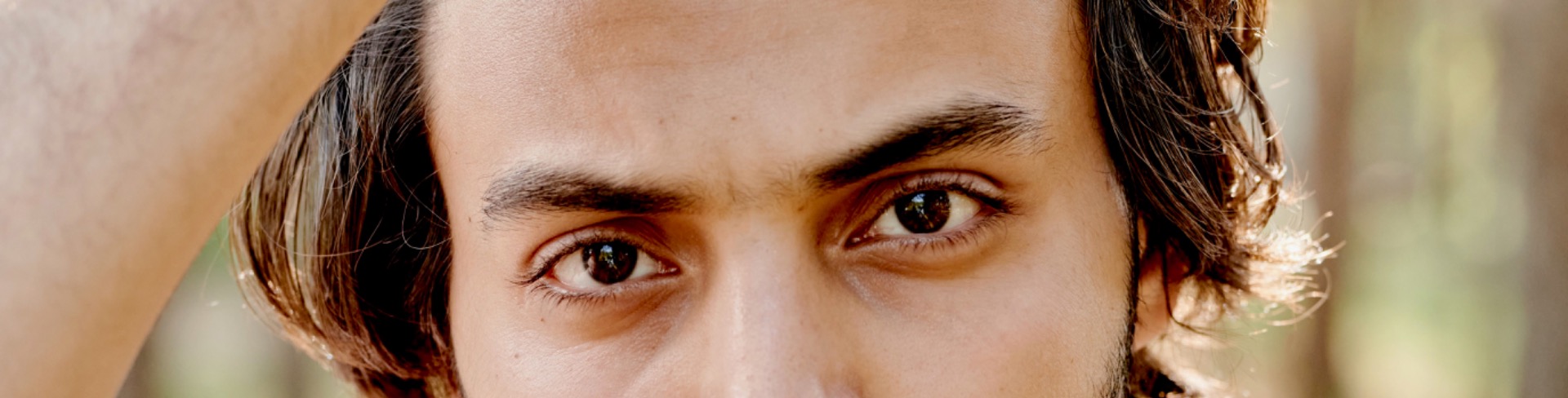 Close-up of a man’s face with focused black masculine eyes, warm sunlight, and softly blurred background.